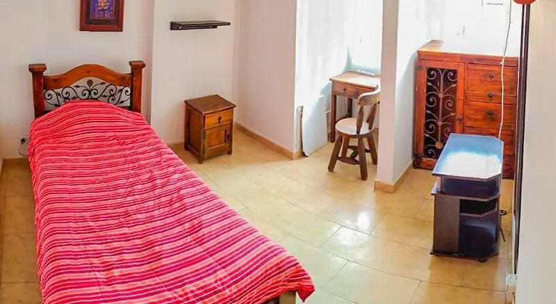 Habitación con cama sencilla, escritorio con silla y cómoda de madera