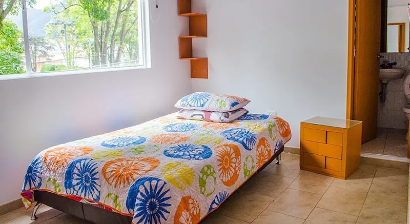Habitación con cama de colores y la puerta del baño al fondo